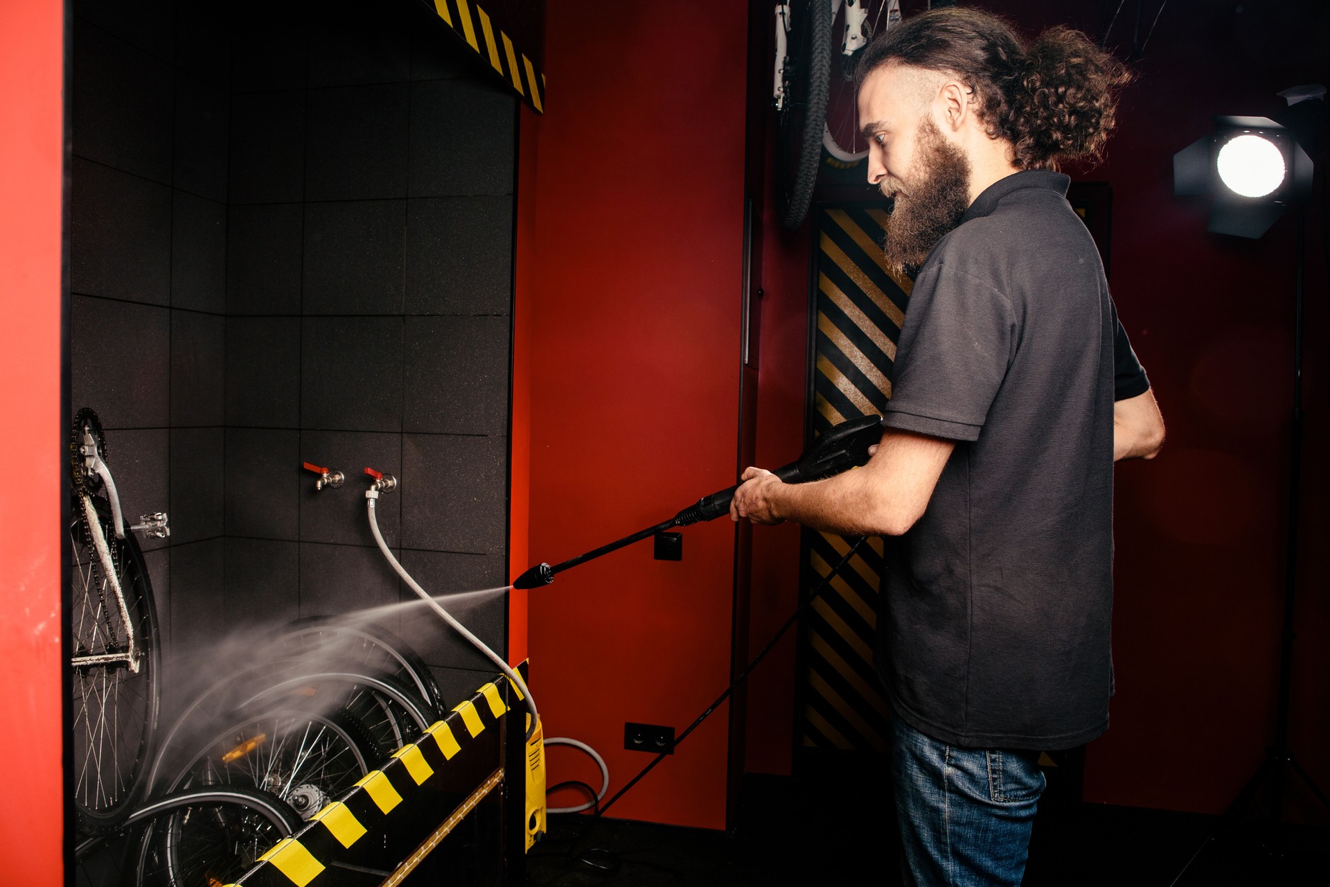 Services professional washing of a bicycle in the workshop. Close-up of hand Young Caucasian stylish man doing bicycle cleaning using automatic electric water pump. Sprays scatter from the pressure